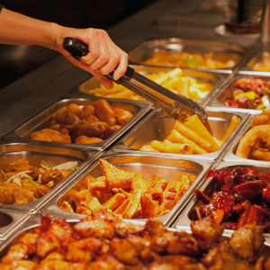 Close up of Chinese buffet food with someone picking a pancake roll